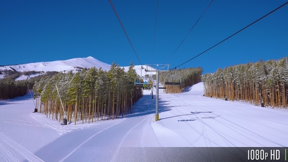 Backside view of skiers and snowboarders riding a ski lift up the mountain