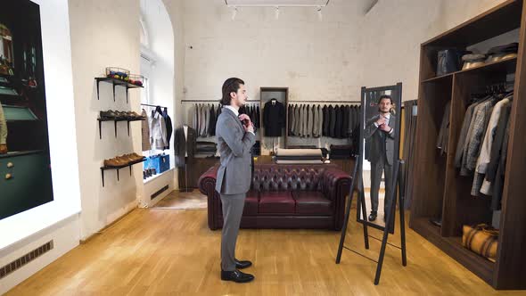 Young man trying on suit and tie in front of mirror in classy boutique.