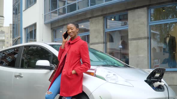 African American Woman Talking Phone While Charging Electric Car