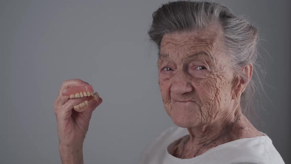 Removable Denture in Hands of Senior Patient in Studio on Gray Background