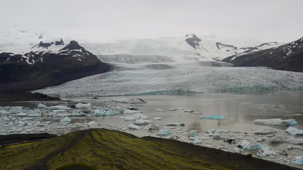 Iceland glacier with green hills and blue ice with drone video moving in.