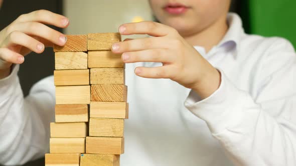 close-up playful caucasian boy 6-7 years old builds a tower from wooden blocks at home.