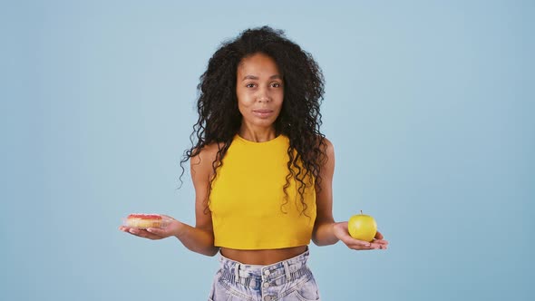 Afroamerican Lady is Smiling and Taking Out an Apple and a Donut From Behind Her Back Thinking What