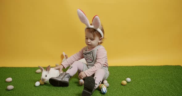 A 2Yearold Child is Playing with Rabbits on a Green Carpet with Colored Eggs