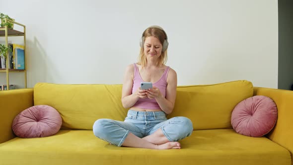 Happy and Cheerful Woman in Pink Tank Top and Blue Jeans Sits on Bright Yellow Sofa at Home and