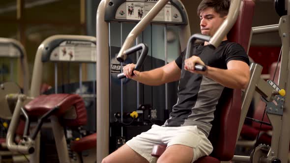 Closeup of teen bodybuilder doing vertical chest press exercises on a machine at a fitness gym.