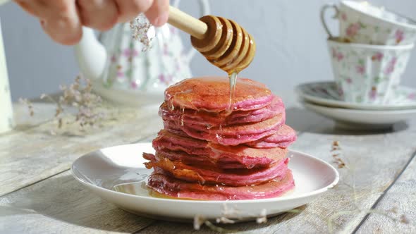 Hand Pouring Honey on Stack of Pink Beet Pancakes