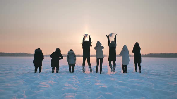 A Group of Girls Friends are Jumping and Throwing Snow Up at Sunset