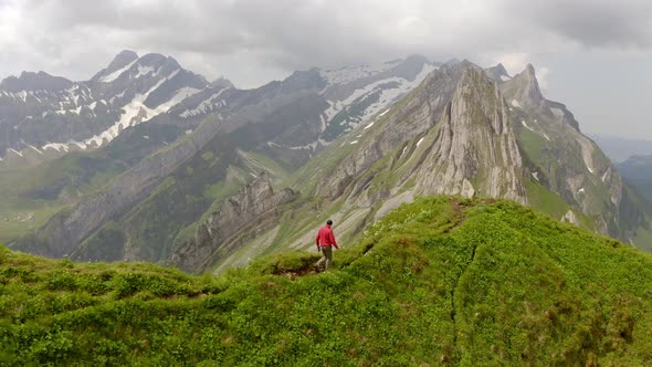 A man in a red jacket is walking on top of a mountain.The man is doing a hero pose at the end of the