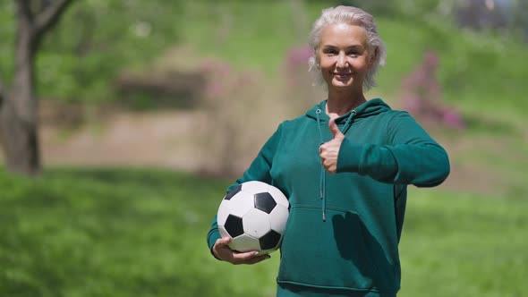 Portrait of Joyful Caucasian Senior Woman Holding Soccer Ball Showing Thumb Up Smiling