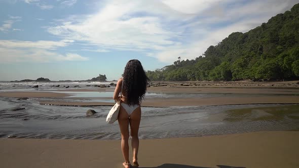 Female model in bikini walks away from camera in slow motion on beach