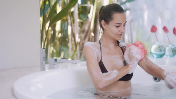 Girl in Bikini Washes Body Taking Bath in Room with Plants
