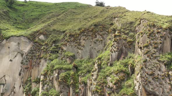 Flying sidewards to show more of a large rocky grey and red coloured cliff covered in bromelias