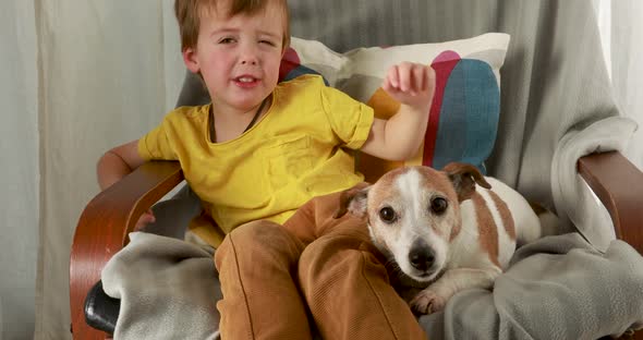 Little Boy Pulls Faces and Pets Dog with Brown and White Fur