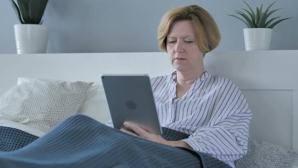 Old Senior Woman Using Tablet while Lying in Bed