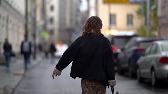 Stylish Woman Listens To Music with Headphones and Walks Around the City in a Public Place, Holding