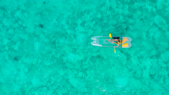 Aerial Top View of Young Woman Kayaking the Floating Transparent Boat on the Crystal Clear Water in