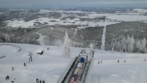Top of ski mountain. Ski lifts, gondola and people skiing. Trees and slopes, everything snowy. Aeria