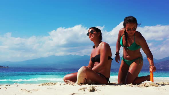 Young smiling ladies on vacation in the sun at the beach on sunny blue and white sand 4K background