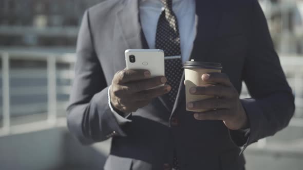 Unrecognizable African American Man with Coffee Cup Surfing Internet on Smartphone. Young Successful