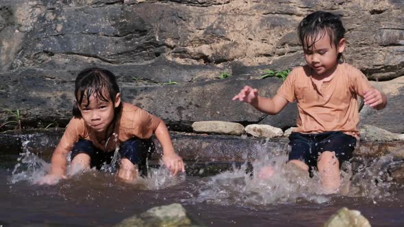 Asian little girl playing in the forest stream with her sister. alt
