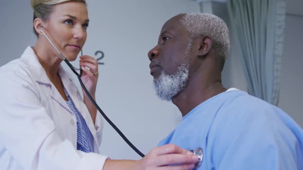 Caucasian female doctor examining african american senior male patient with stethoscope at hospital