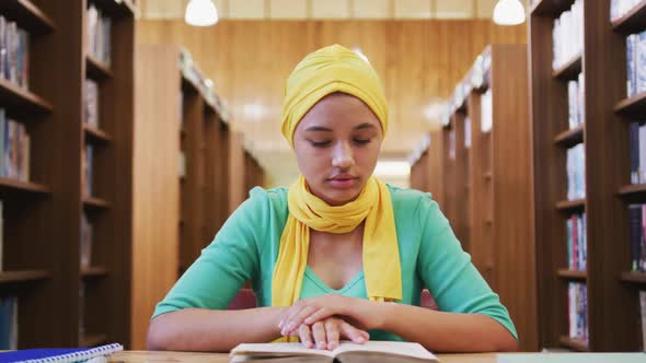 An Asian female student wearing a yellow hijab sitting at a desk and reading a book