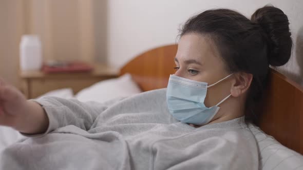 Side View Portrait of Young Unwell Caucasian Woman Lying in Bed Passing Thermometer to