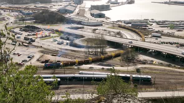 Aerial clip of Freight train slowly moving along tracks amidst a busy highway in Uddevalla Sweden