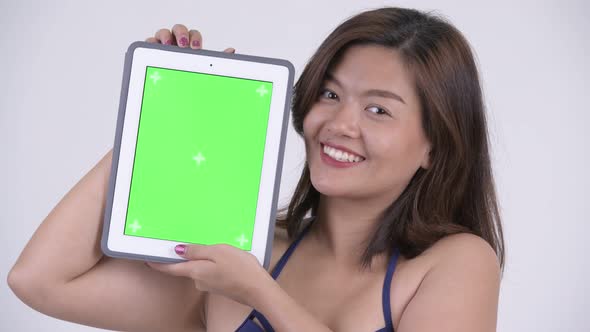 Face of Happy Young Beautiful Asian Tourist Woman in Bikini Showing Digital Tablet