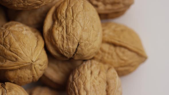 Cinematic, rotating shot of walnuts in their shells on a white surface - WALNUTS 