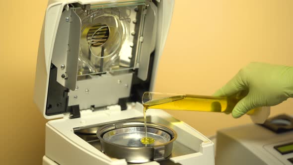 Hand of Laboratory Assistant in a Protective Glove Pouring Oil From a Flask Into an Apparatus for