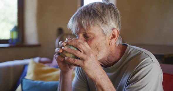 Happy senior caucasian man sitting in living room at home enjoying a cup of coffee