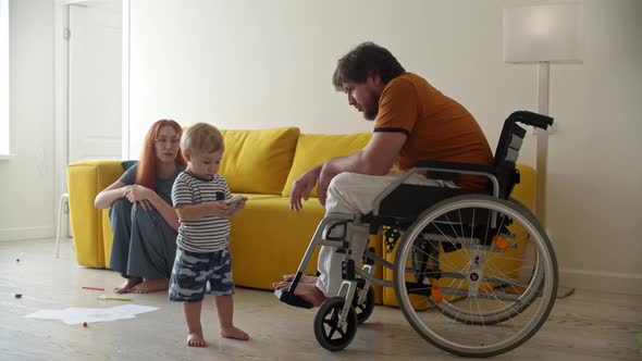 Man in a Wheelchair Helps His Little Baby Son to Fix a TV Remote