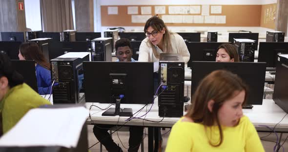 Mature teacher working with multiracial students inside computer classroom at college school