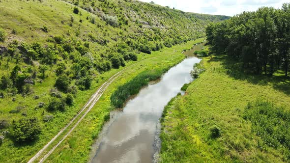 Aerial drone view of a valley in Moldova. River, a lot of greenery, cloudy sky