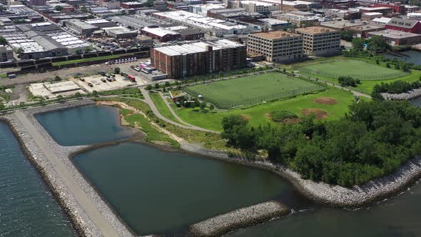 high up dolly shot towards soccer & baseball field over the waters & stone jetty on a clear sunny da