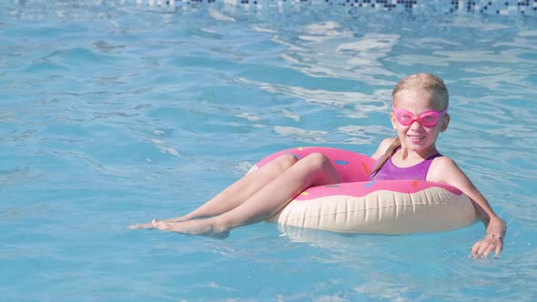 Portrait Smiling Girl in Swimming Pool Child in Swimming Glasses Sitting on Pink Donut Swimming Ring