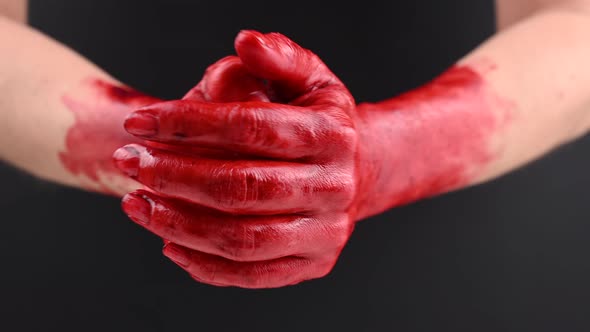 A Woman Rubs Her Hands Stained with Blood on a Black Background