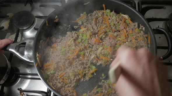 Cooking minced beef in a fry pan on a stove top with onion, celery and carrot. Top down angle.