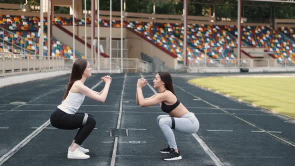 Sportswomen Doing Squats with Resistance Fitness Rubber Band on Stadium