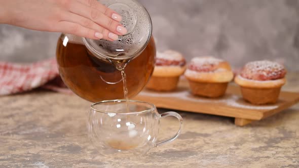 Pour Hot Tea in Glass Cup. A Cup of Tea with Roses Buns, Sweet Buns with Sugar Powder.