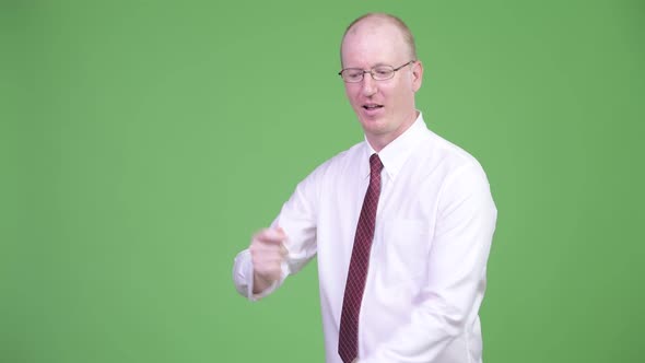 Happy Mature Bald Businessman Snapping Fingers and Showing Something