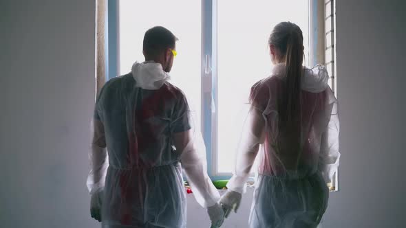 Positive Couple in Protective Wear Joins Hands Near Window