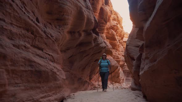 Hiker Walking On Dry Curve Riverbed In Deep Slot Canyon With Orange Smooth Rocks