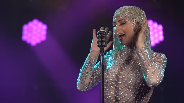 A Young Woman in a Chic, Tight-fitting Jumpsuit with Rhinestones and a Shiny Headdress Dances Near a