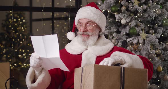 Charming Kind Santa Claus Holds a New Year's Gift Box Nods His Head Directing His Gaze From the