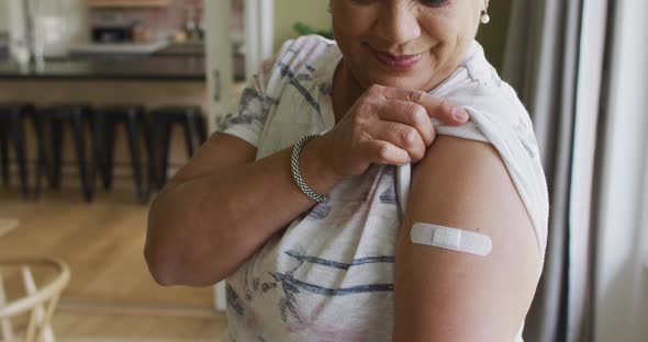 Happy mixed race senior woman showing plaster on arm after covid vaccination