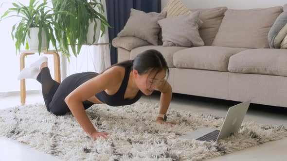 Young fit asian woman in sportswear watching online video with fitness exercises on laptop and doing