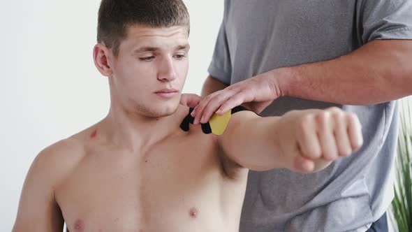 Physiotherapist Placing Kinesiology Tape on Shoulder of Athlete in Clinic